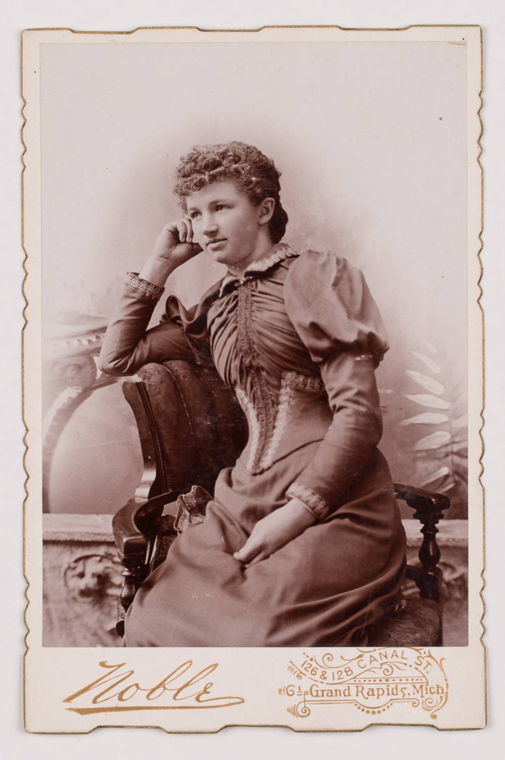 Antique photograph of young woman reclining in chair resting face in hand wearing 19th century style dress